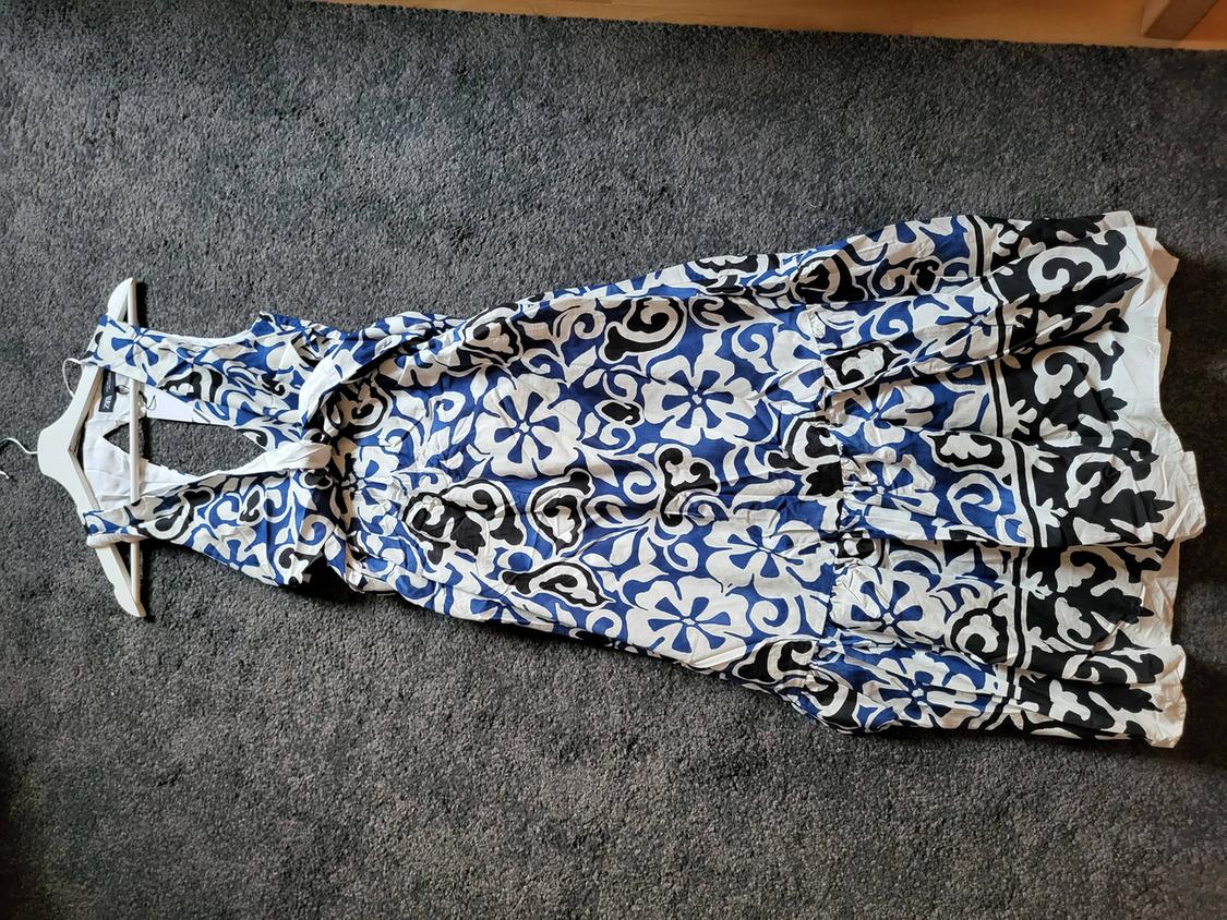 Sleeveless floral print dress in blue, black, and white, on a hanger against a grey carpet.