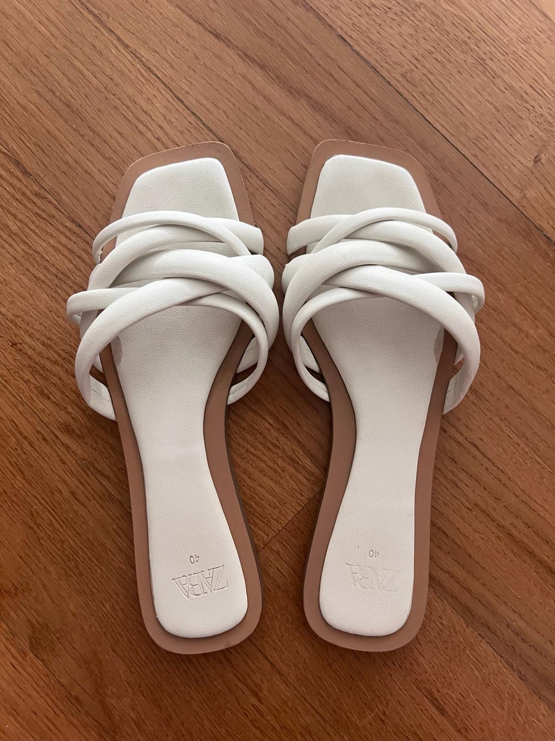 White flat cross-strap sandals on a wooden floor. Text in the image: ZARA 40.