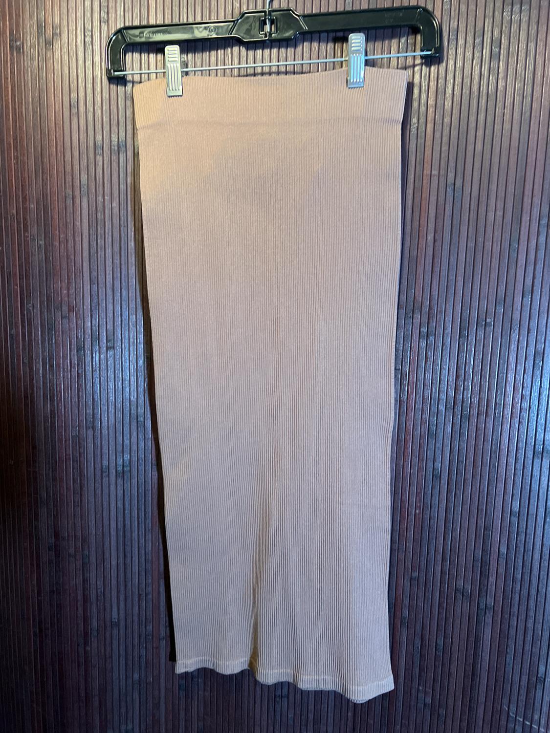 Long beige knit skirt hanging on a black hanger, dark wood wall background with vertical texture.