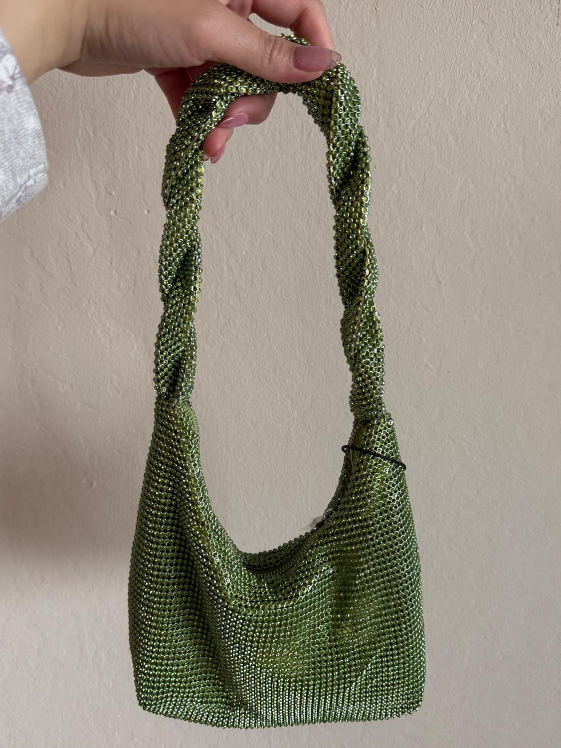 A bright green handbag with a braided handle, held by a hand with pink painted nails, against a beige background.