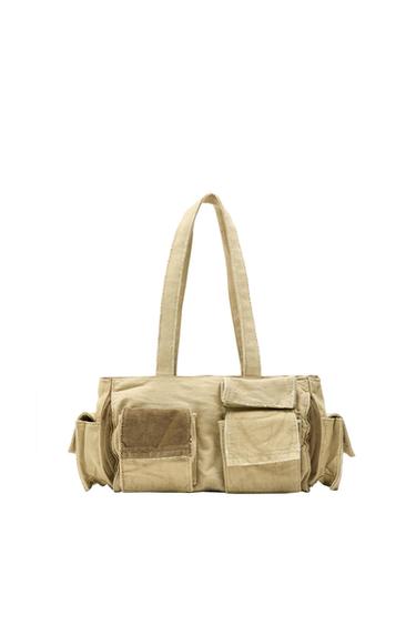 Beige canvas tote bag with multiple pockets and long handles. White background, utilitarian style and functional design.