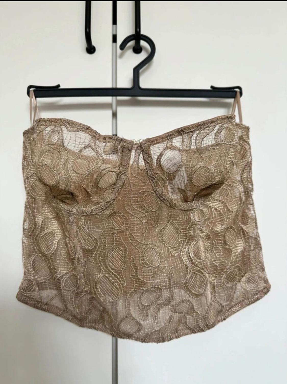 Beige semi-sheer corset top with thin straps and lace design, hanging on a black hanger against a white background.