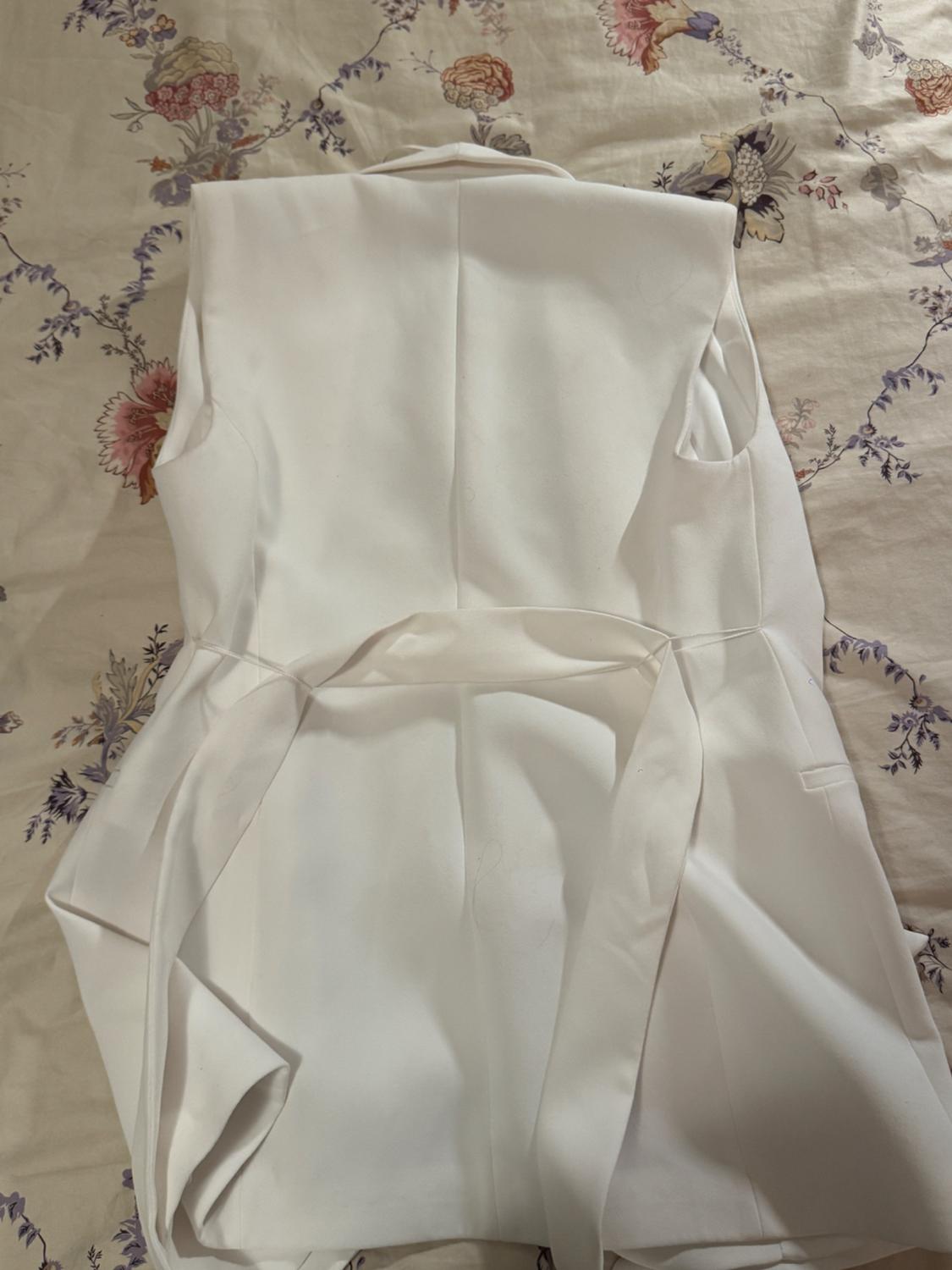 White sleeveless vest on a floral-print quilt in pastel tones. The fabric has a smooth and elegant finish.