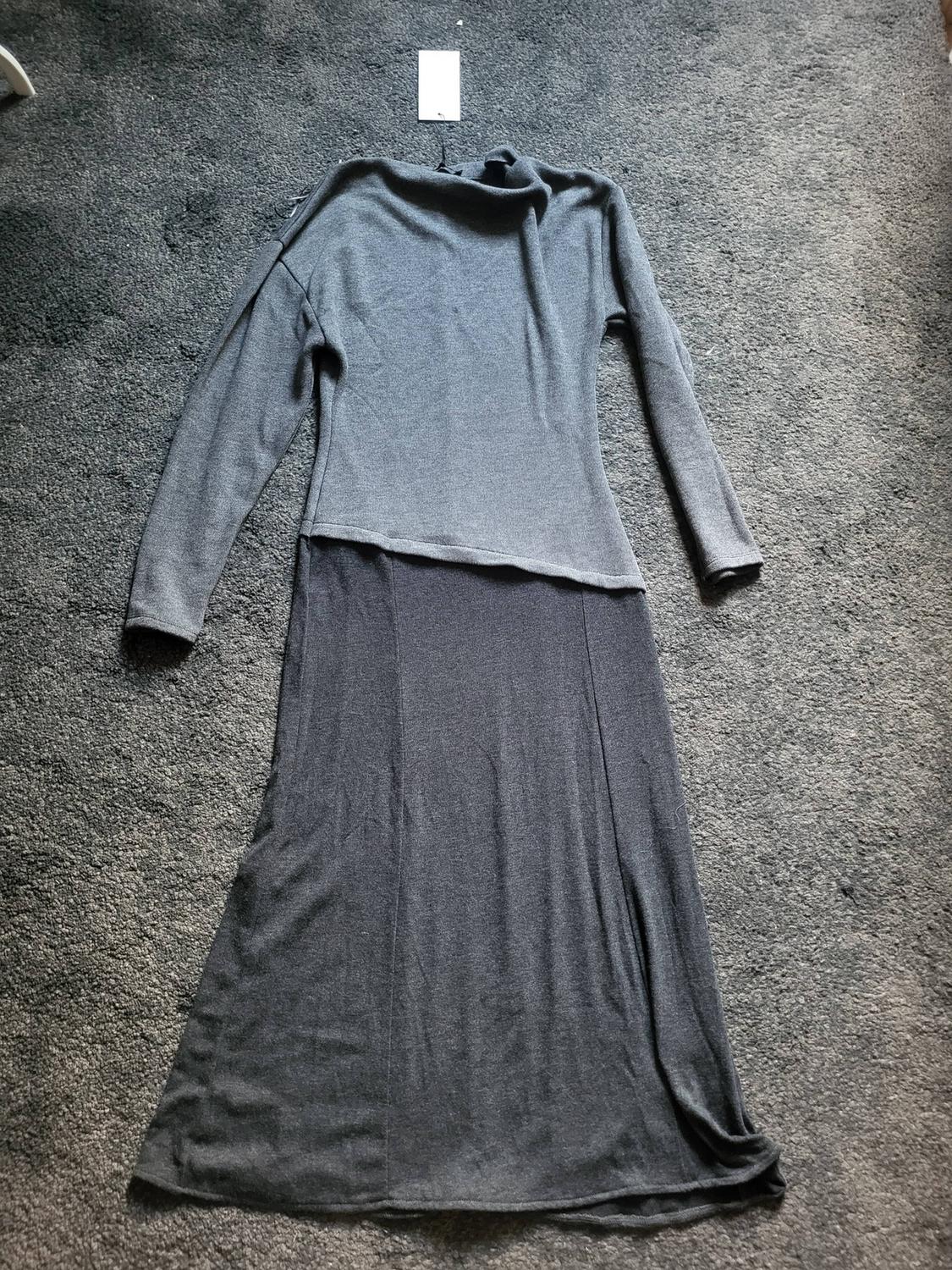 Grey long-sleeved, high-necked dress laid out on a grey rug. White label visible at the top.