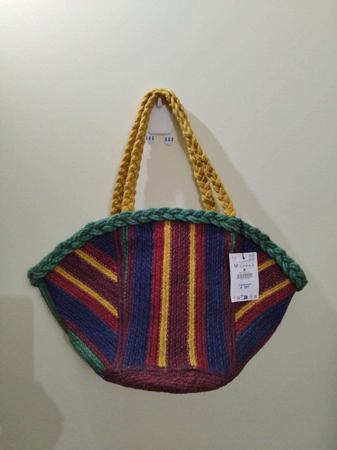 Braided bag with blue, maroon and yellow stripes, green trim and yellow handles, hanging on a white wall. Label with text M € 39.