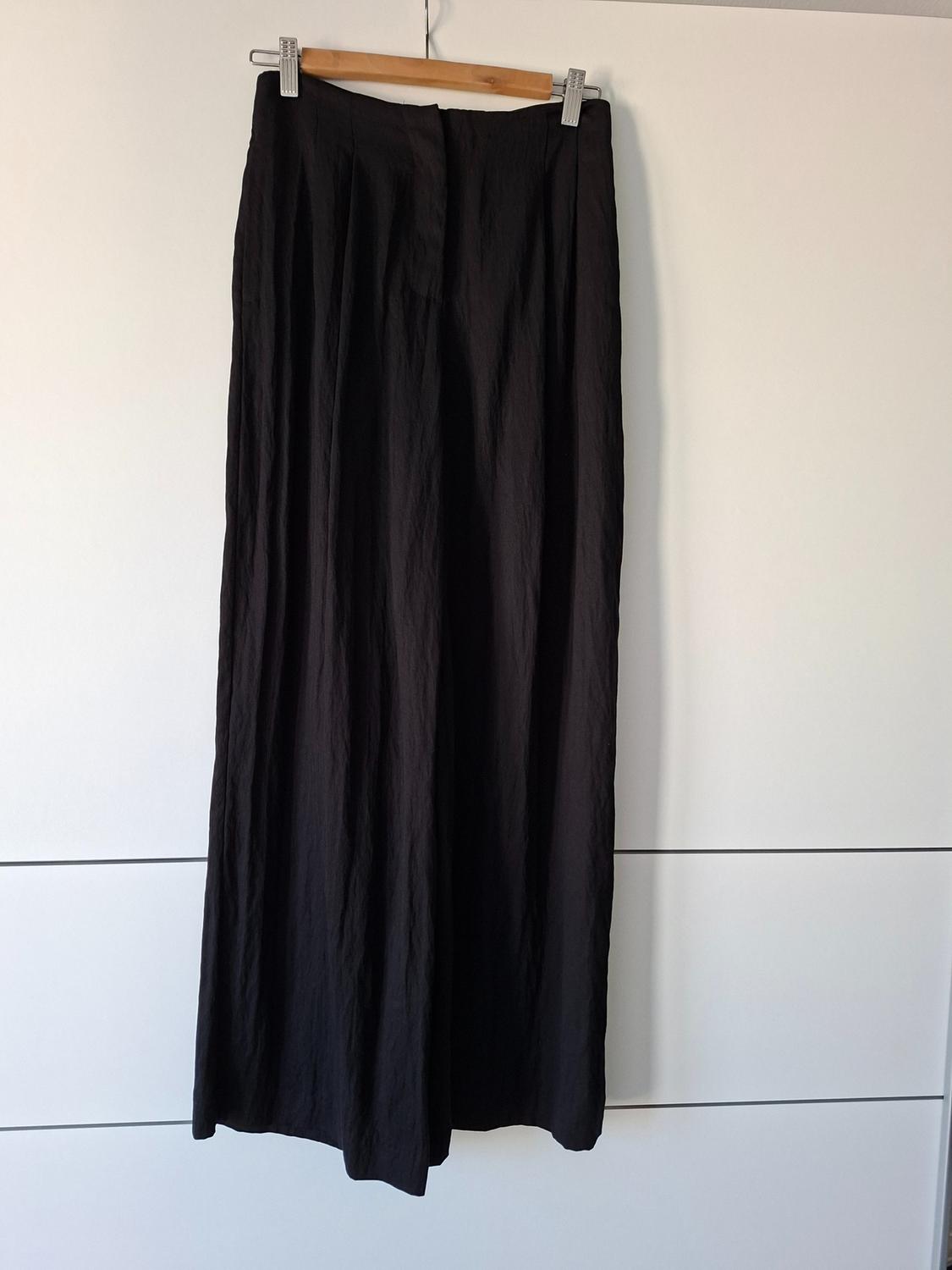 Black wide-leg trousers hanging on a wooden hanger against a white background.