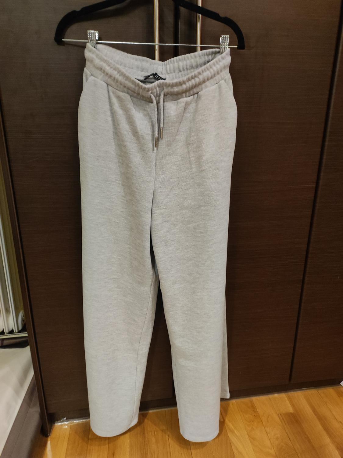 Grey jogging bottoms hanging on a black hanger against a dark wood background, on a light wood floor.