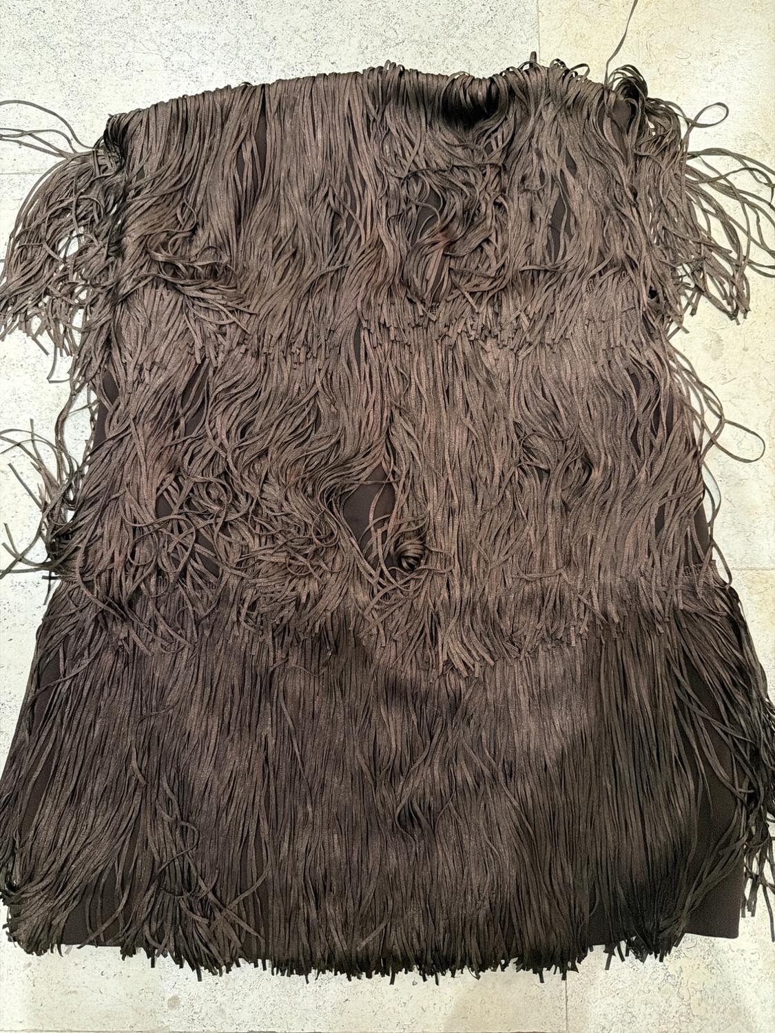 Dark brown garment with long cascading fringe, spread out on a light stone surface in a relaxed composition.