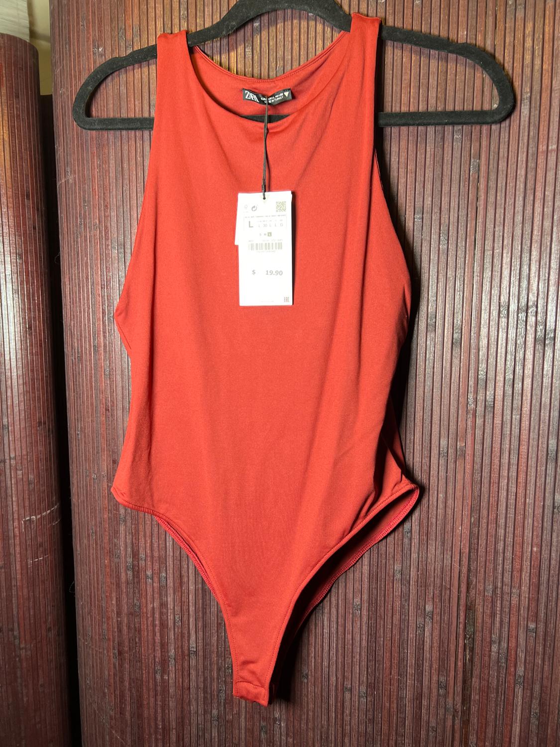 Sleeveless red bodysuit hanging on a black hanger against a wooden background. Visible tag with a price of $19.90.