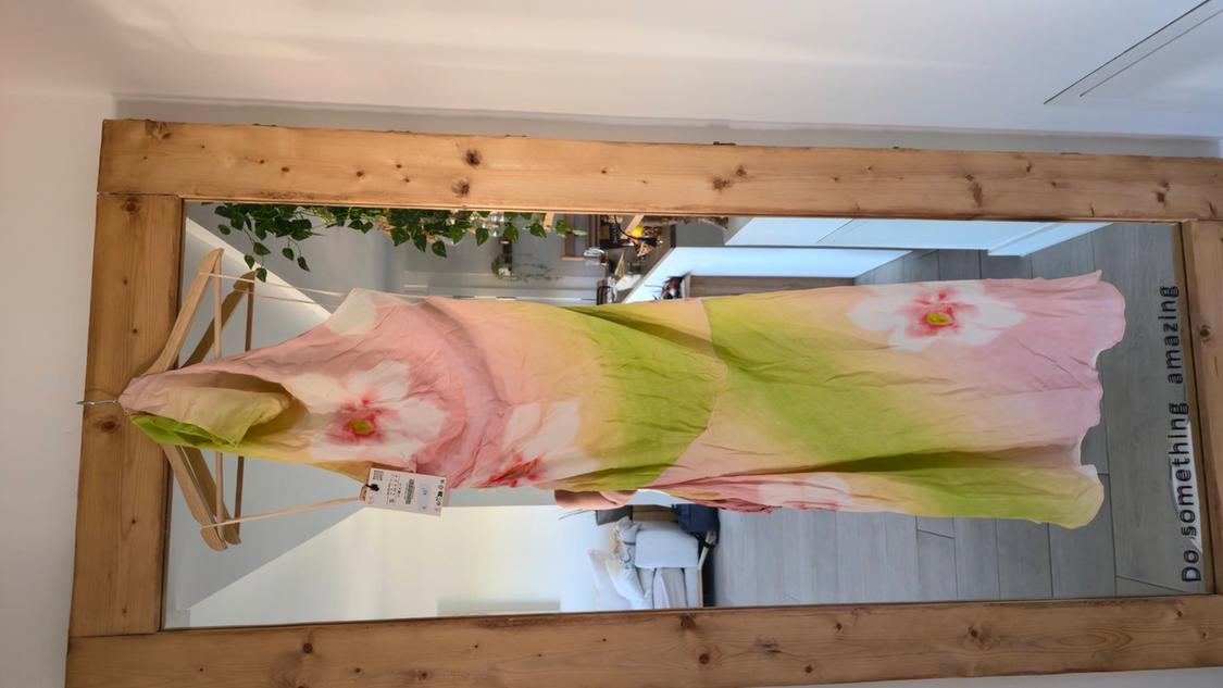Pink and green floral dress hanging on a wooden mirror reflecting a room. Text on the mirror: Do something amazing.