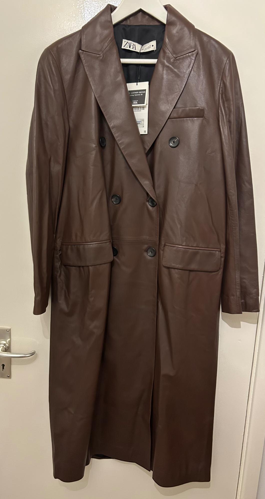 Brown leather coat hanging on a white hanger, with black buttons and a visible ZARA brand label.
