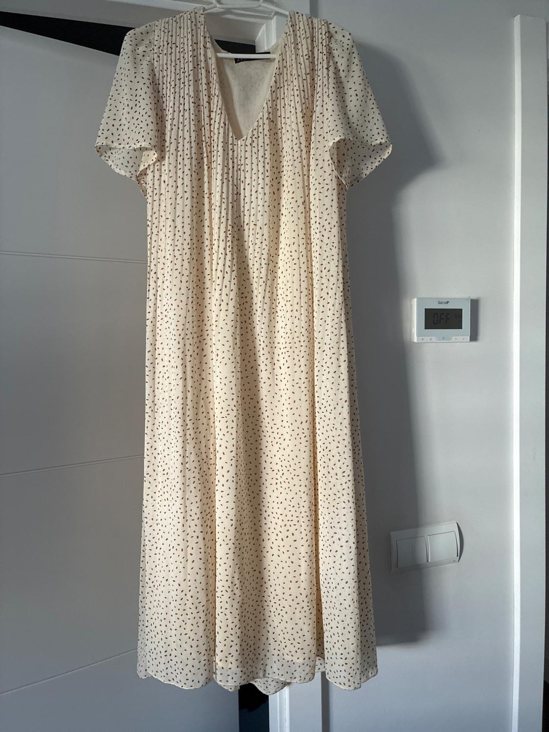 Light-coloured dress with dark spots, short sleeves and a V-neck, hanging on a white door. On the wall, a thermostat displaying the text OFF.