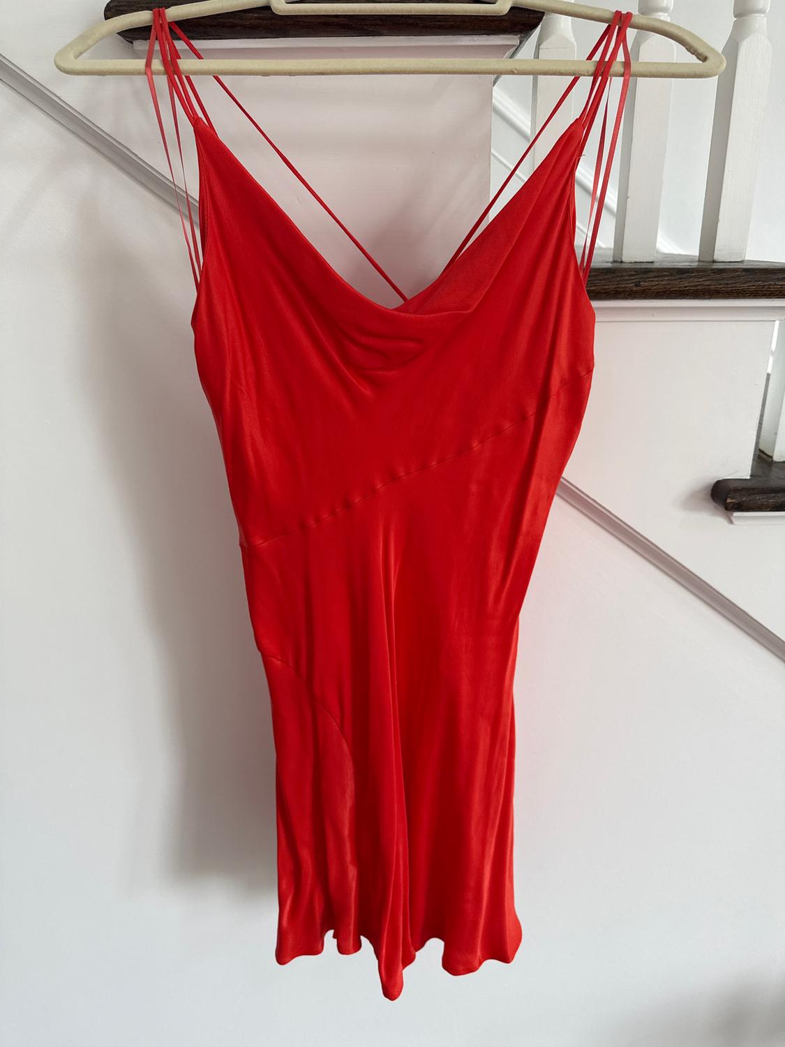 Red spaghetti strap dress hanging on a hanger against a white background, showcasing an elegant and flowing design.