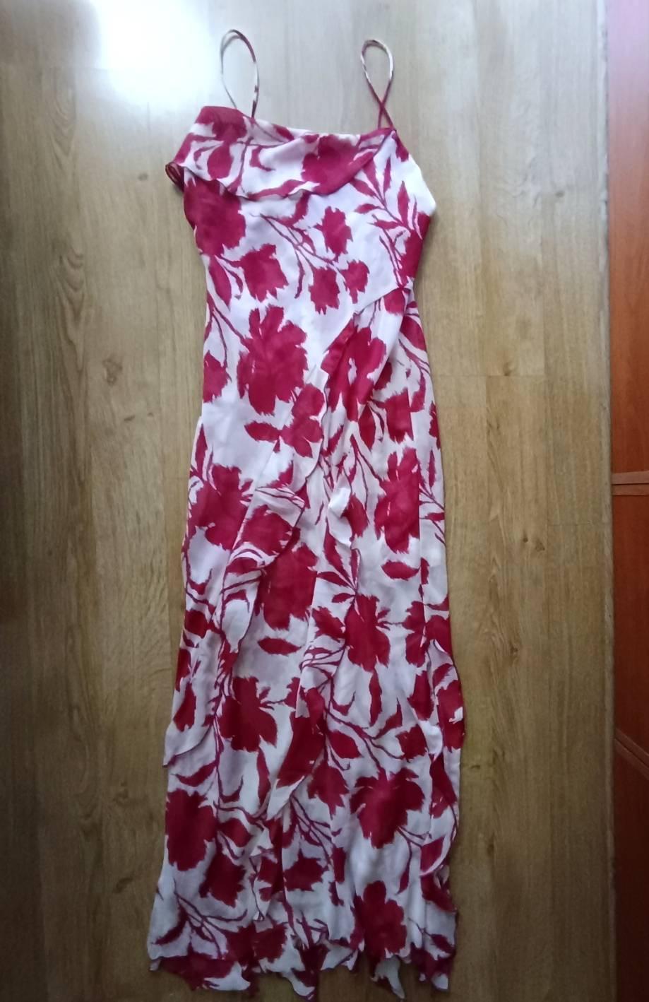 White maxi dress with a red floral print, thin straps and asymmetric ruffles, laid on a wooden floor.