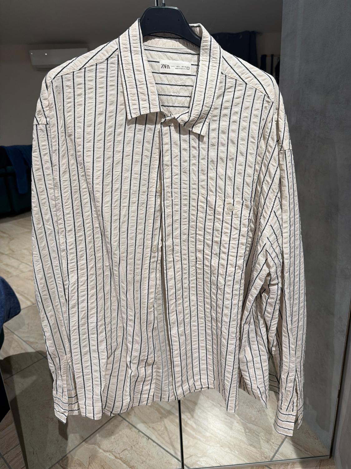 Black and white vertically striped shirt hanging on a black hanger. Room background with tiled floor.
