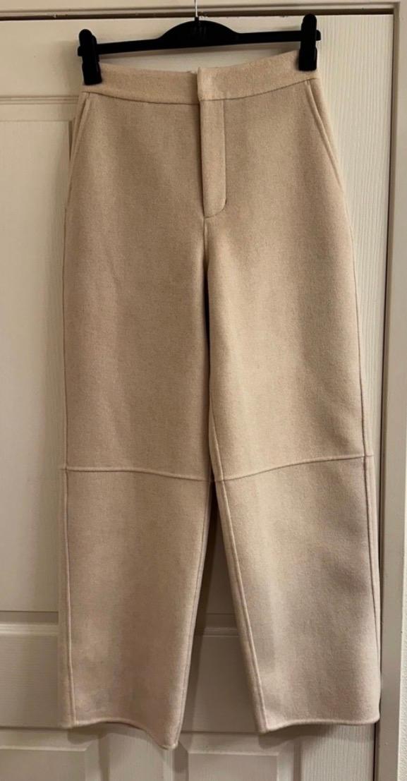 Beige pants hanging on a black hanger over a white door. Simple design with visible stitching on the legs.