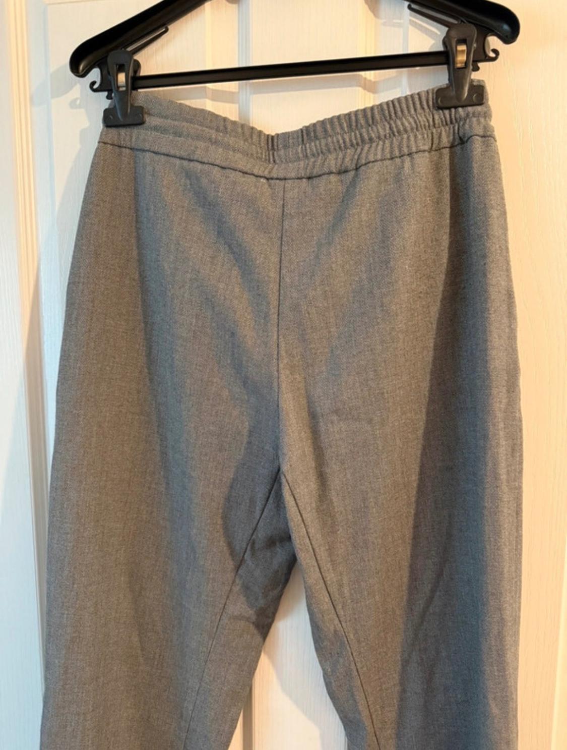 Grey trousers hanging on a black hanger over a white door. Lightly textured fabric and elasticated waist.