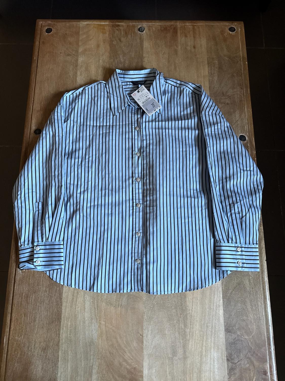 Light blue long-sleeved shirt with dark vertical stripes, laid out on a wooden table in a relaxed composition.