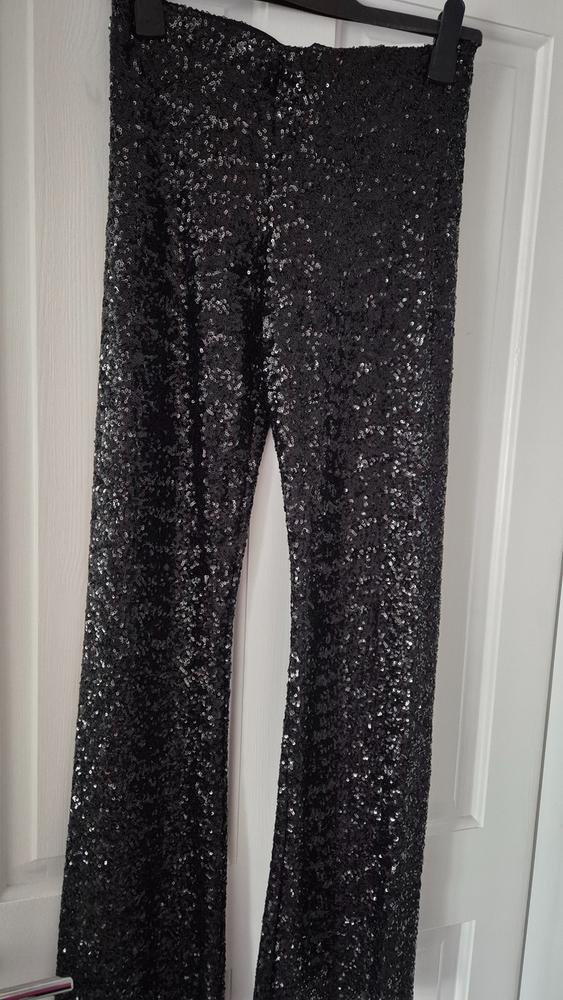 Black sequined trousers hanging on a hanger over a white door.