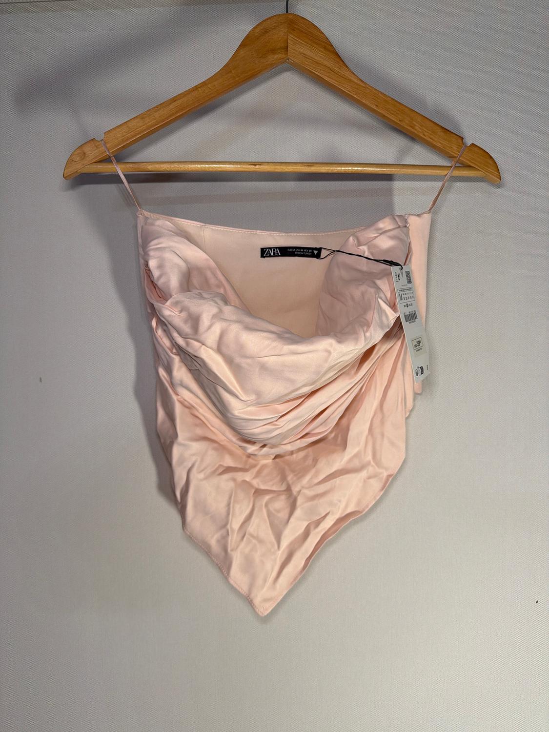 Light pink camisole top hanging on a wooden hanger. Visible tag with the ZARA brand. White background.