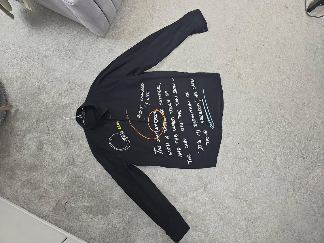 Black long-sleeved shirt with white and orange text: "BIG SUN" and phrases about summer and freedom. It is on a grey rug.