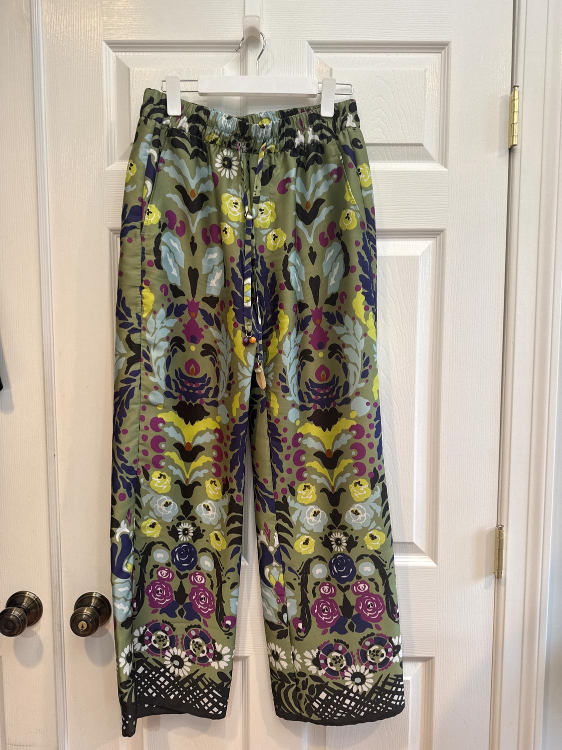 Floral print trousers in shades of green, purple and yellow, hanging over a white door with metal handles.