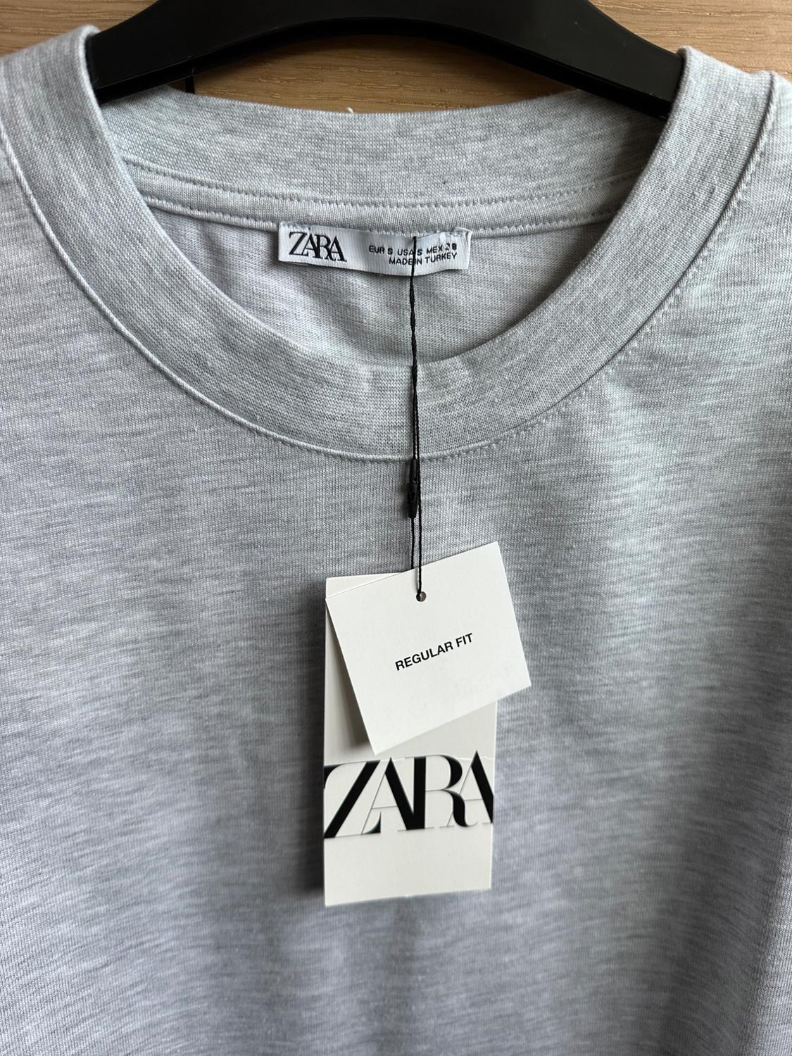 Grey regular fit T-shirt hanging on a black hanger. Visible label with the text "ZARA" and "REGULAR FIT".