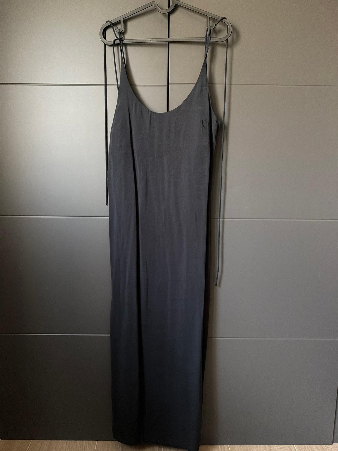 Long black slip dress hanging on a hanger against a dark grey background.