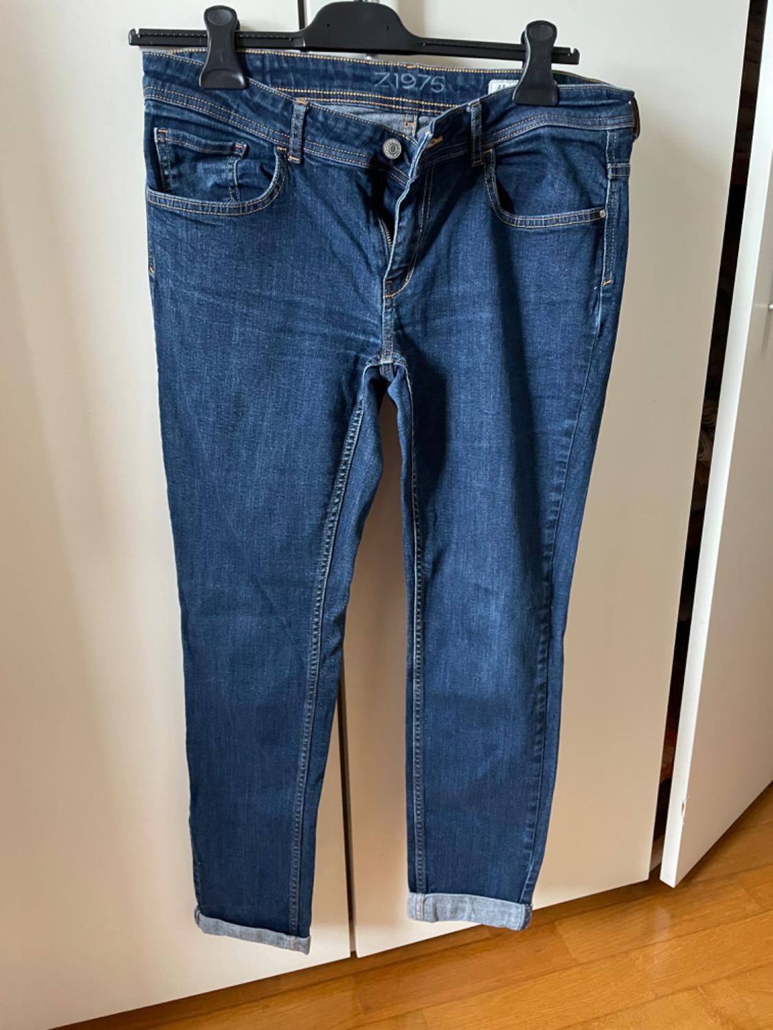 Front view of blue denim jeans with front and back pockets, visible seams, and rolled-up hem.