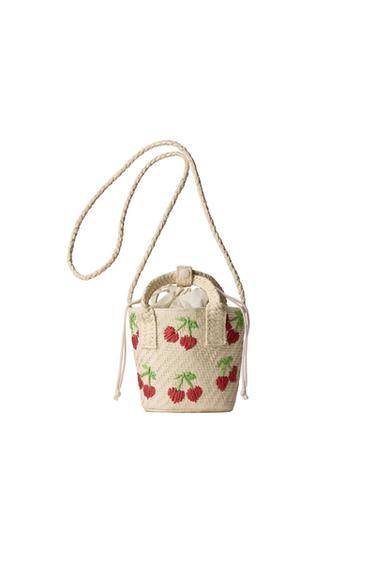 Front view of a straw bag with a red and green cherry print.