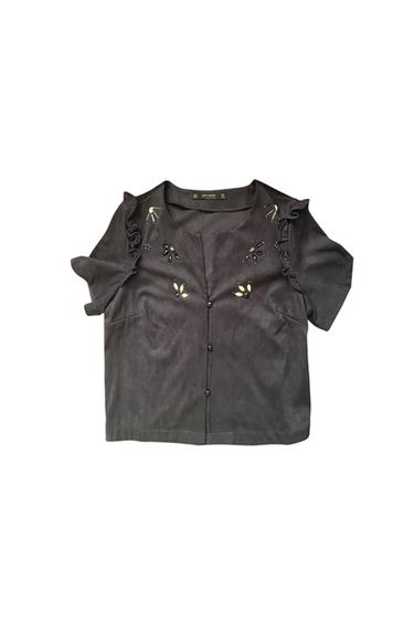 Front view of black blouse with buttons and embroidered details on the chest and shoulders, short sleeves with ruffles.