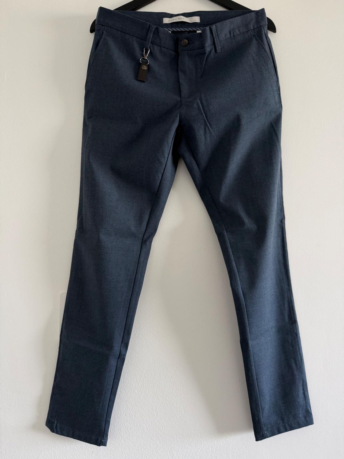 Dark blue pants hanging on a black hanger against a white background. Detail on the belt loop and ZARA MAN text on the label.