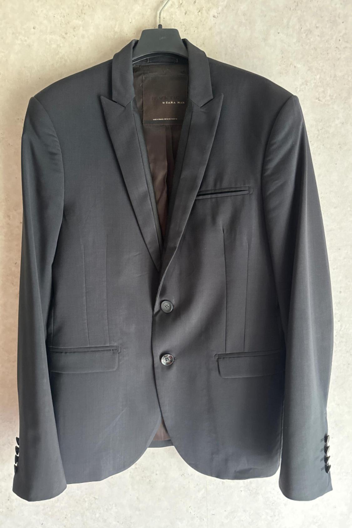 Front view of a black jacket with lapel, two buttons and side pockets.