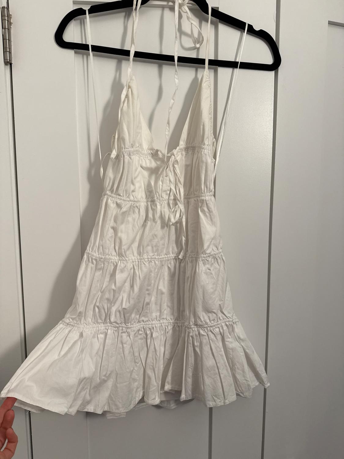 White spaghetti strap dress hanging on a black hanger over a white door. The fabric has a ruched design and ruffles.
