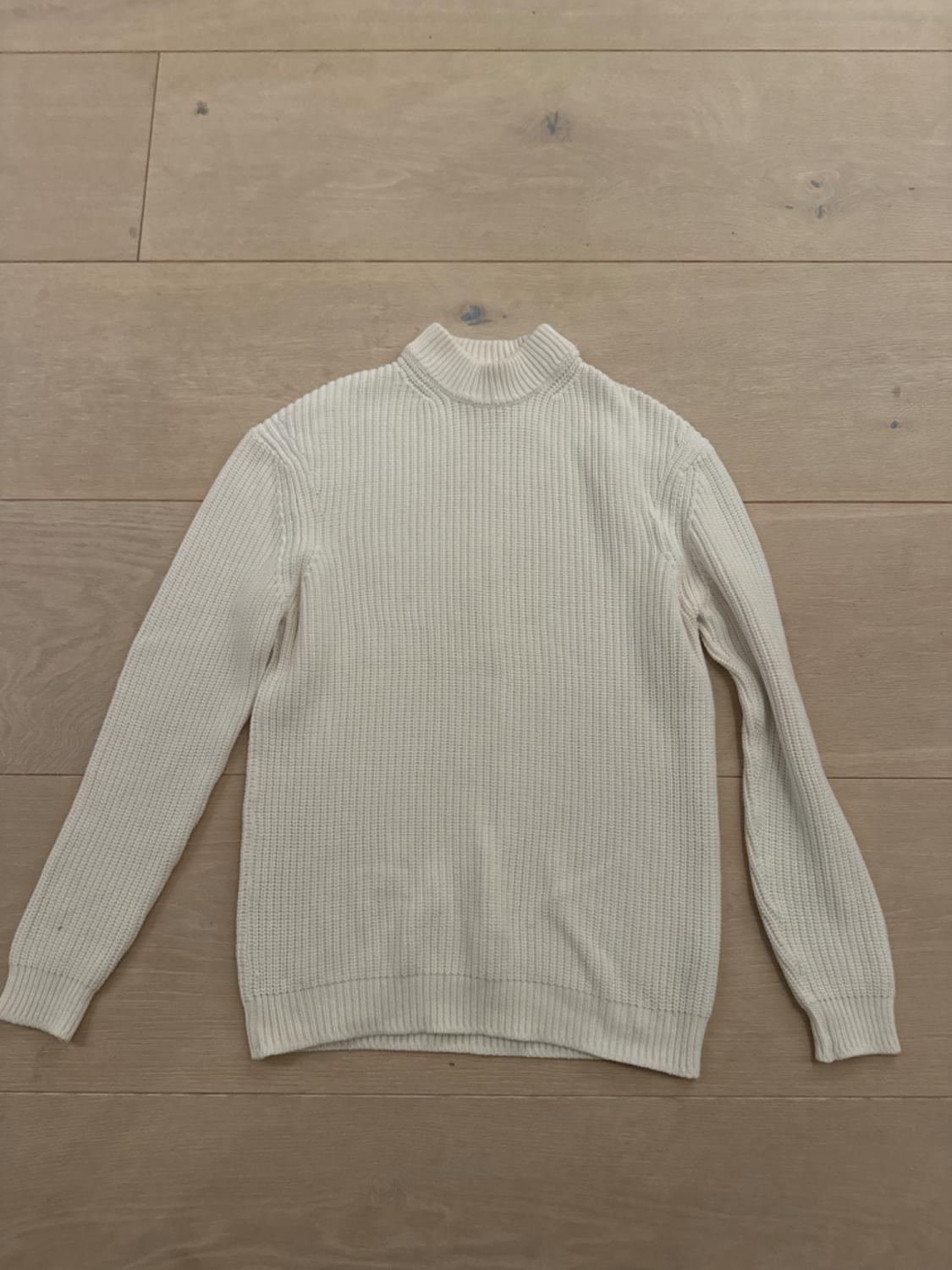 White knitted jumper with a high neck, long sleeves, on a light wooden floor.