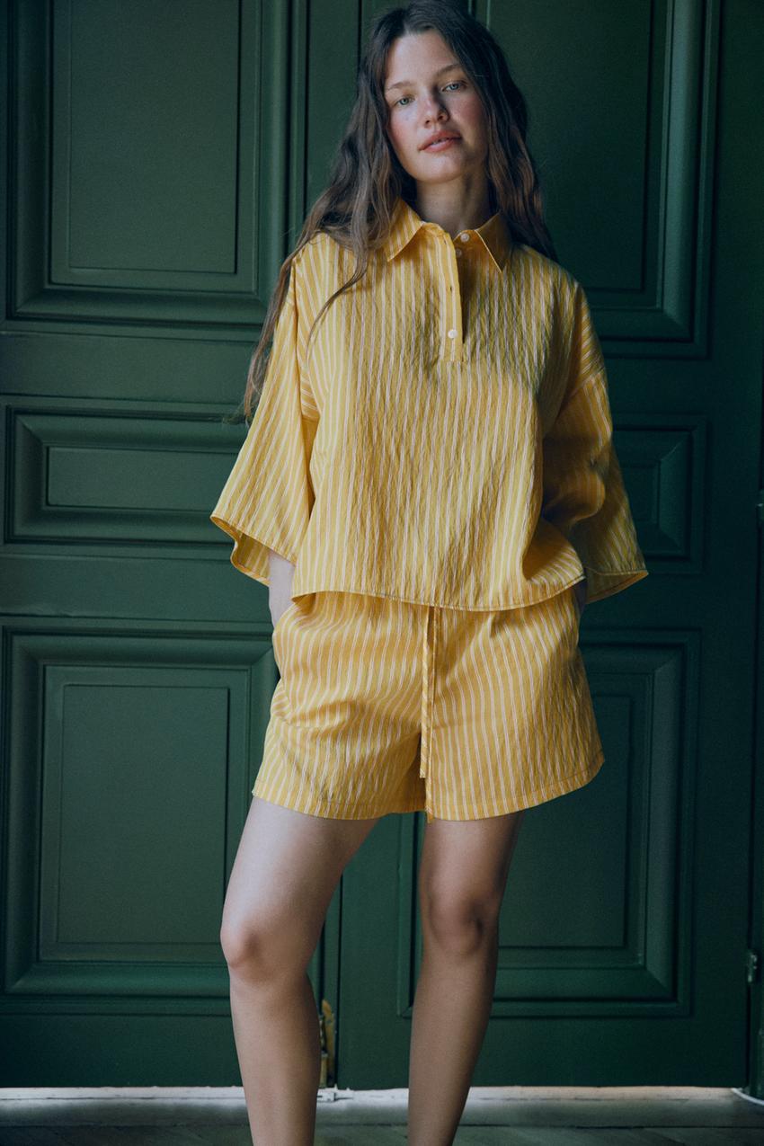 Short-sleeved, half-button shirt set with elastic waist Bermuda shorts, tie detail, and side pockets. Yellow with white stripes.