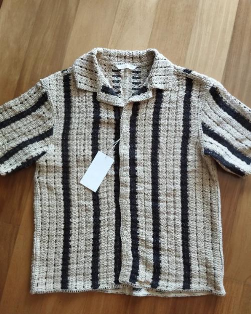 Knitted top with black and beige vertical stripes on a wooden background. White tag hanging from the collar.