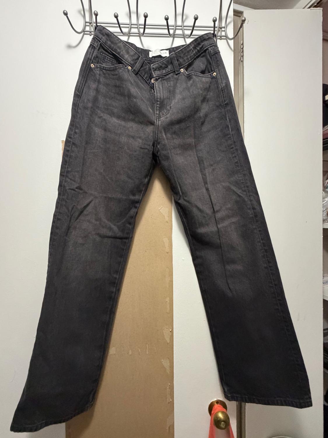 Dark gray washed denim jeans with a straight leg, hanging from a metal hanger on a white door.