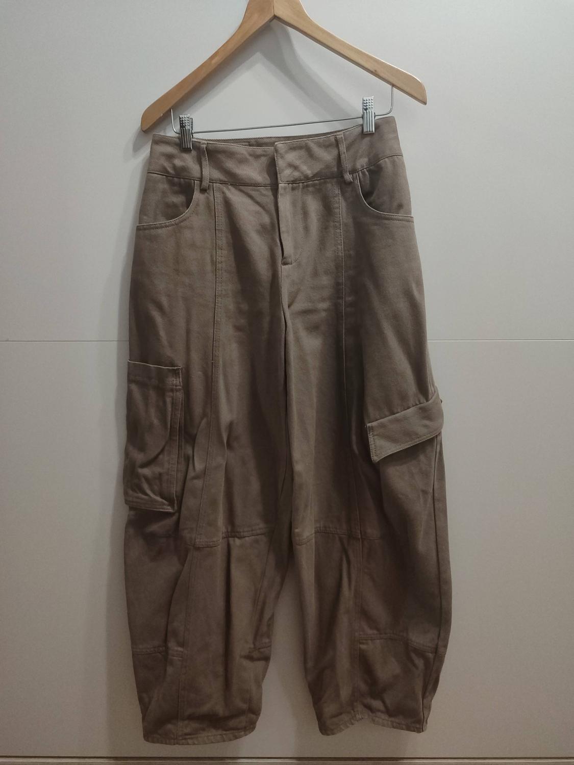 Light brown wide-leg cargo trousers hanging on a wooden hanger against a white background. They feature large side pockets.