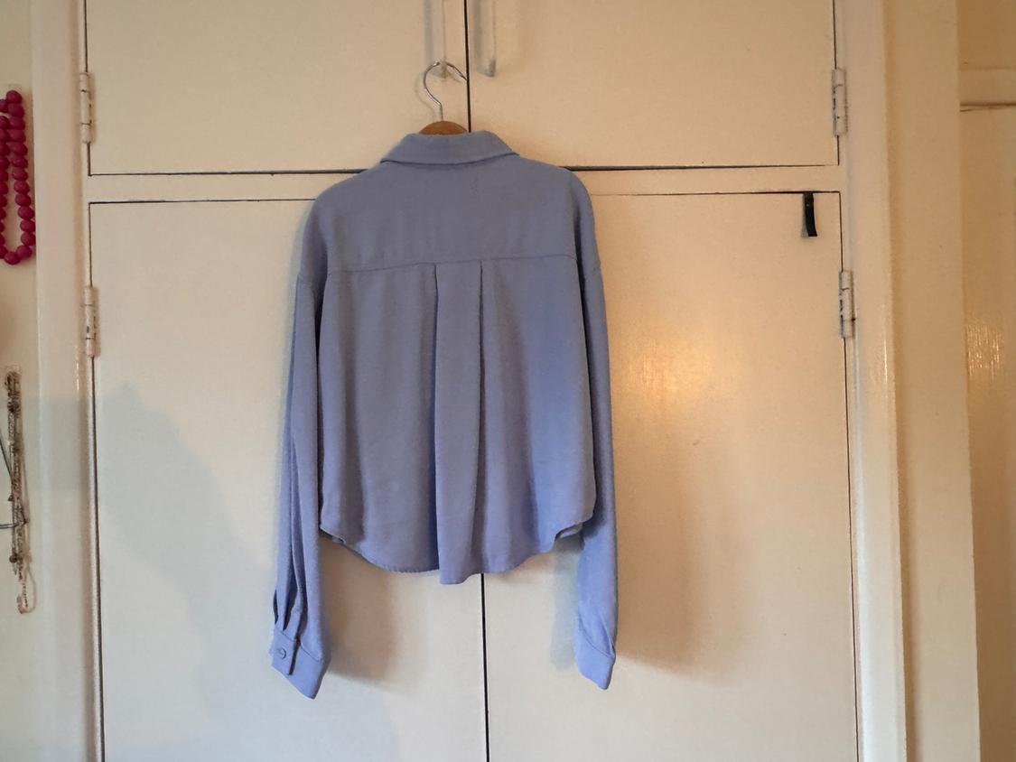 Light blue shirt hanging on a white door. The shirt has long sleeves and a simple design. Homely atmosphere.