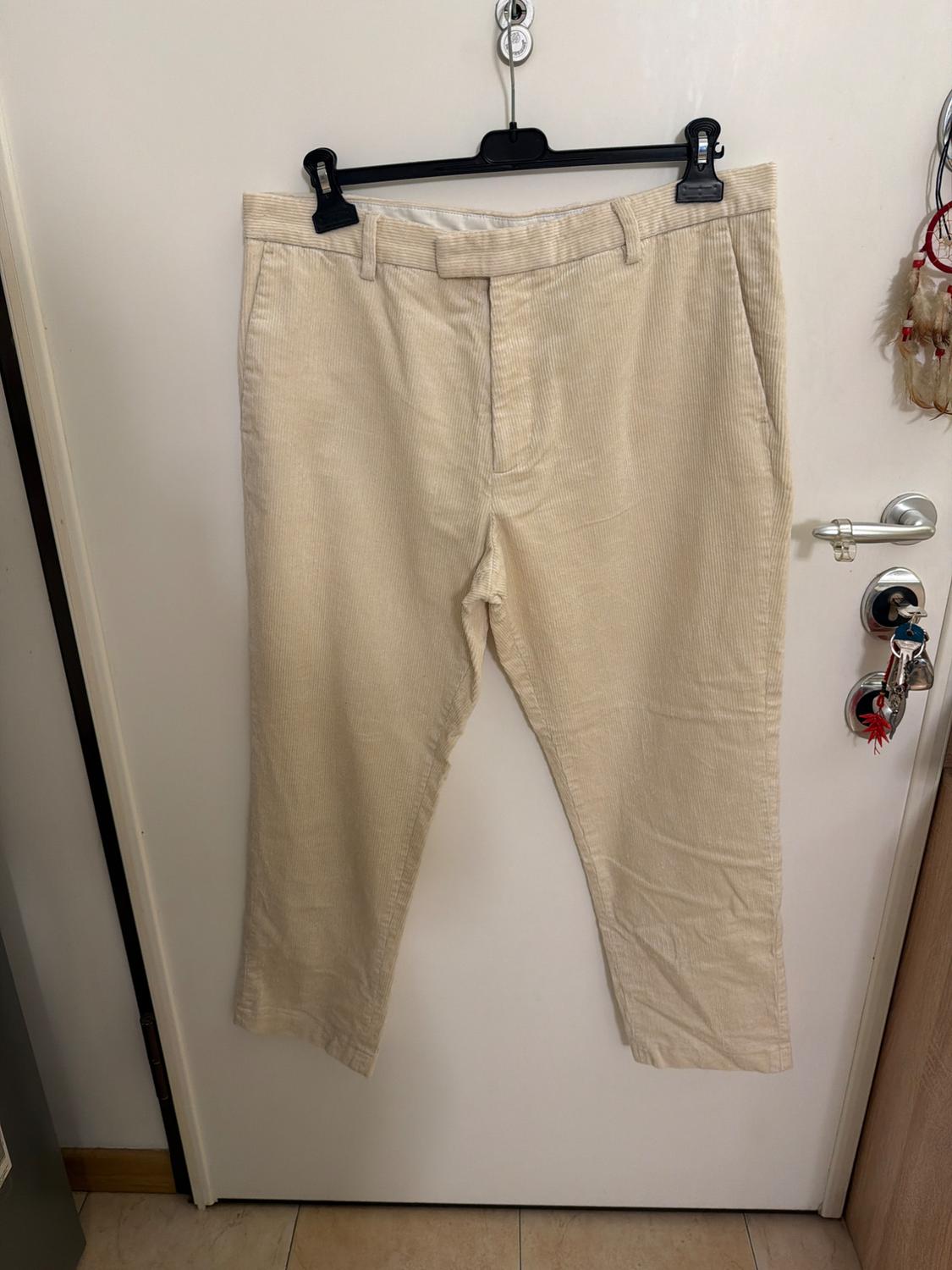 Light beige corduroy trousers hanging on a black hanger over a white door with keys, in a relaxed, homely setting.