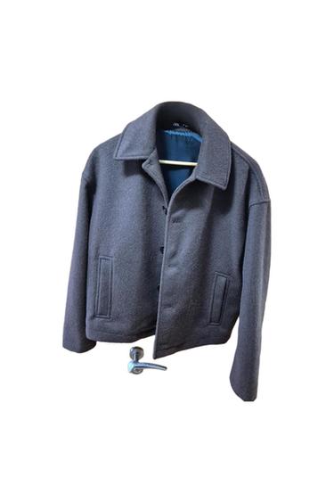 Dark grey jacket hanging on a hanger, with wide lapels and front pockets. White background.