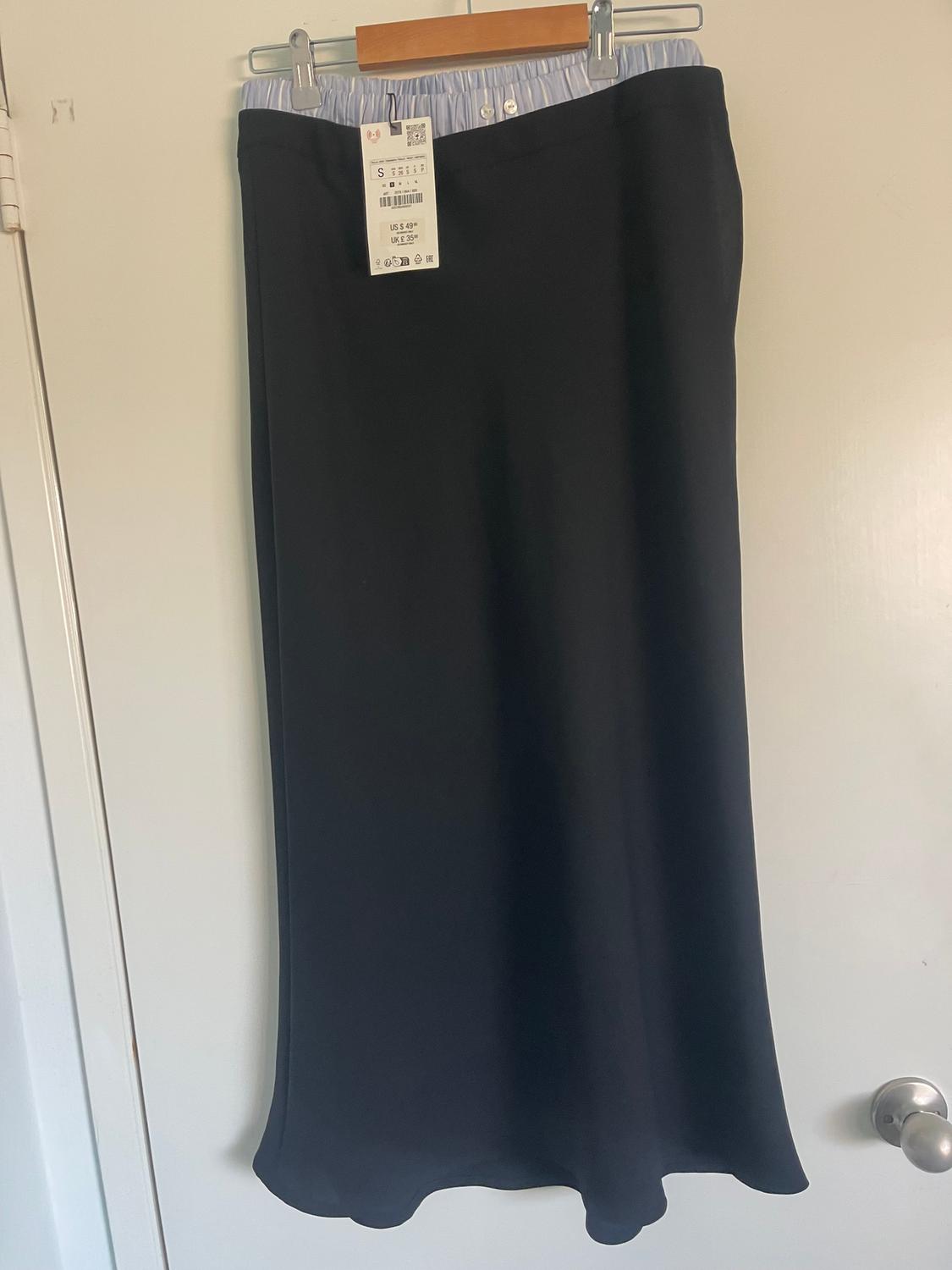 Long black skirt hanging on a hanger, with a visible tag showing size S and price US $59.90. White door background.