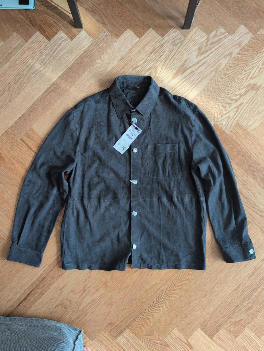 Dark grey long-sleeved shirt with white buttons, a front pocket and a label bearing the text 149, on a wooden floor.