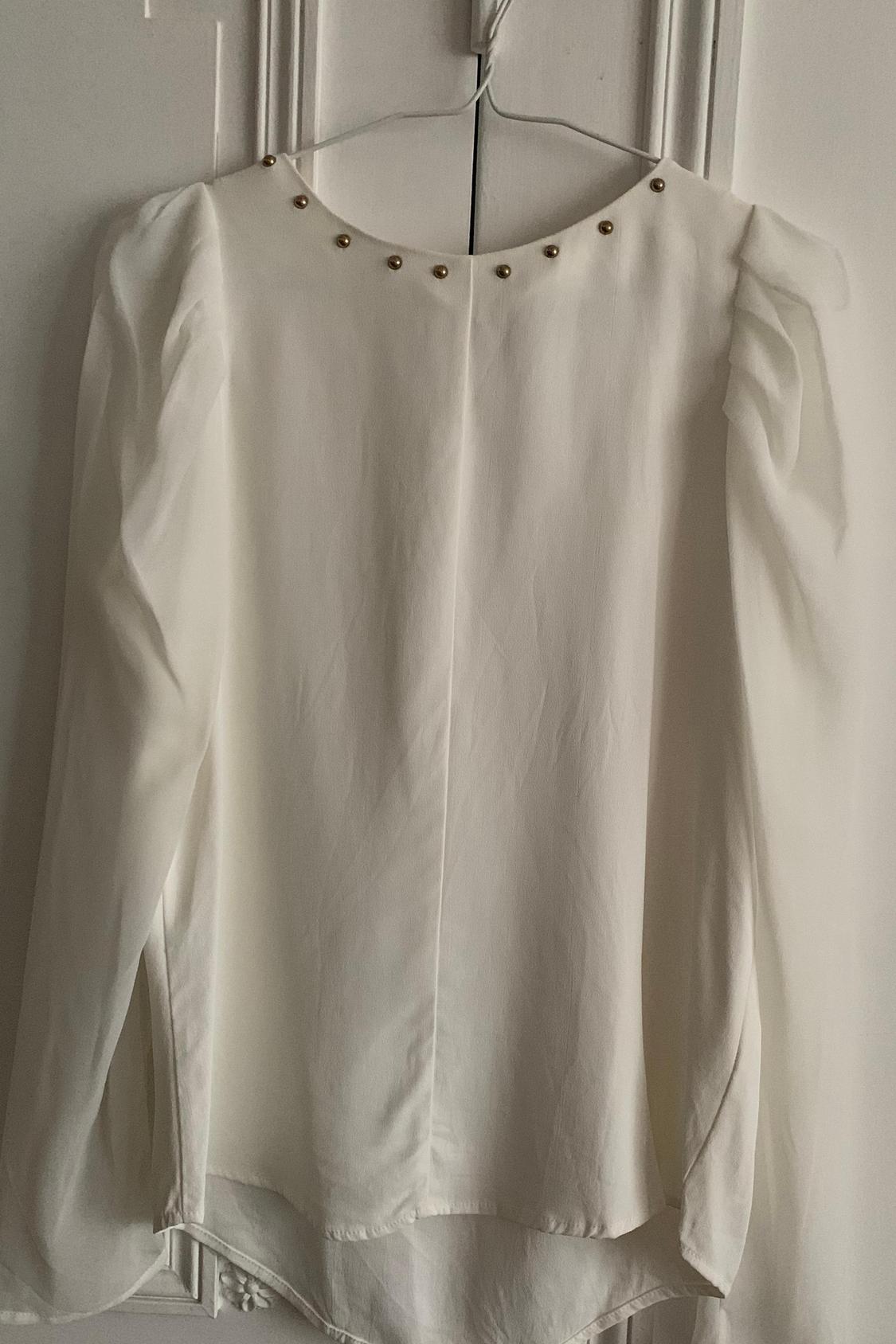 Front view of a white blouse with a round neck decorated with gold buttons.