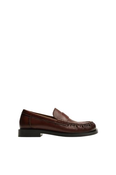 Side view of a dark tan loafer with a black sole and visible stitching.