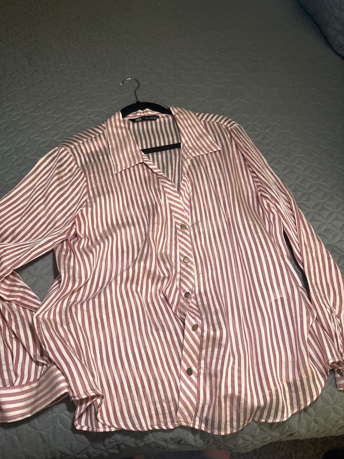 Red and white vertical striped shirt with gold buttons, hanging on a hanger over a gray comforter.