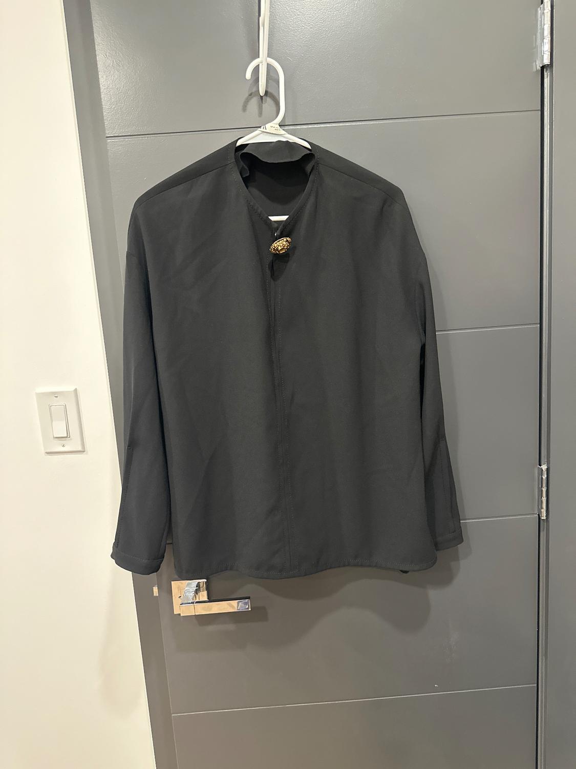 Black shirt hanging on a white hanger over a gray door. It has a gold brooch on the collar.