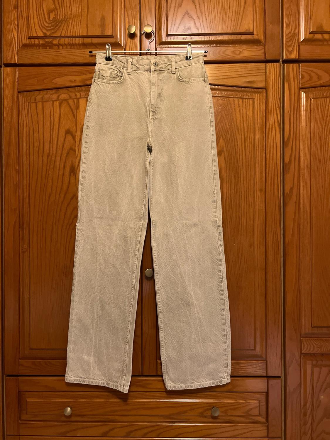 Beige straight-leg jeans hanging on a metal hanger in front of a panelled wooden wardrobe.
