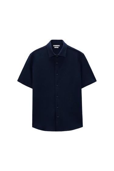 Navy blue short-sleeve shirt with a classic collar and front buttons. Visible tag on the inside of the collar. White background.